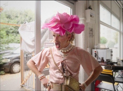 Une drag queen en tenue rose et chapeau fleuri