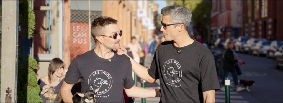Deux hommes en t-shirt Les Pros de l’Immo discutent dans une rue passante